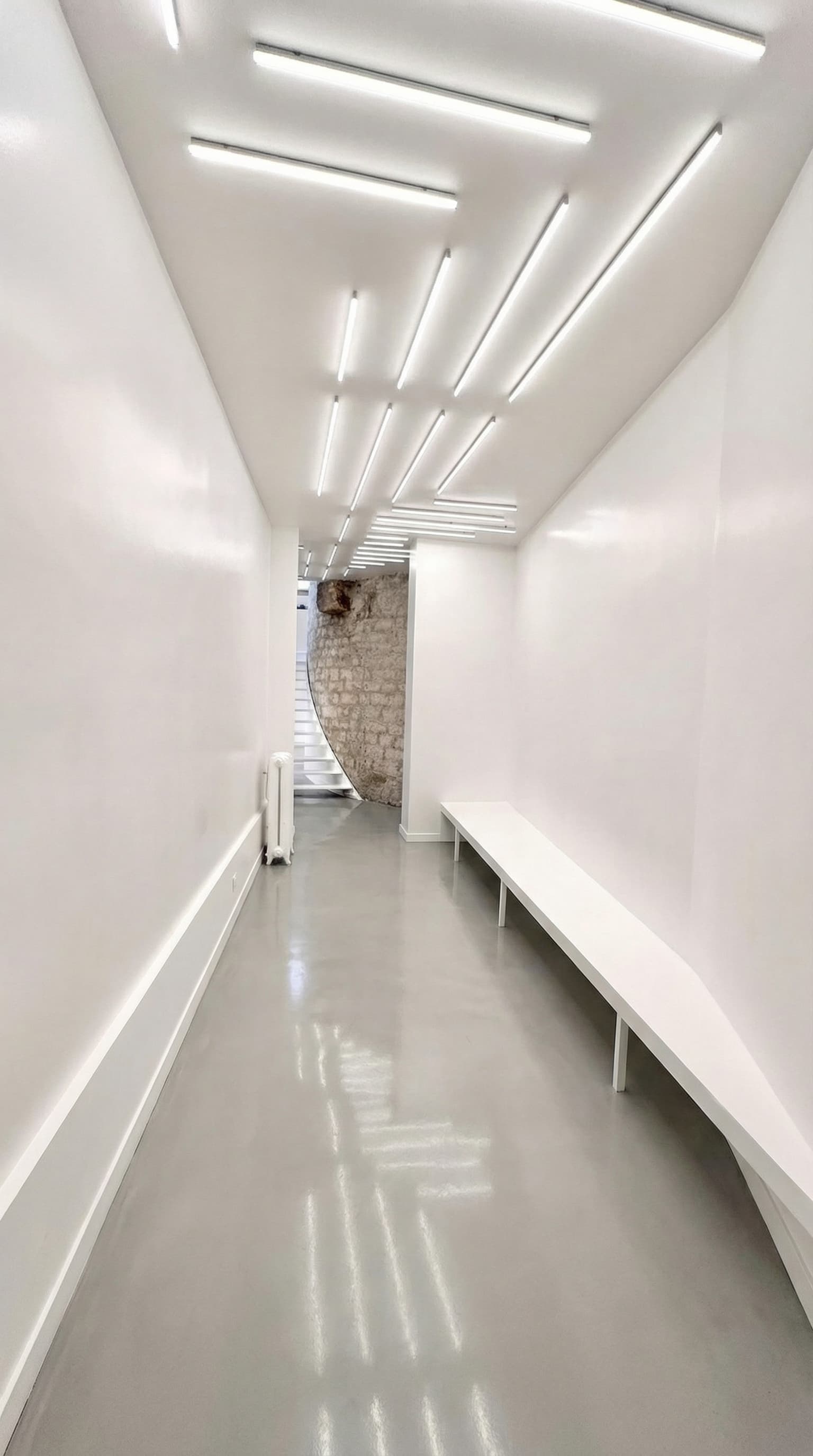 Corridor blanc sous néons graphiques avec banc filant et mur en pierre — Loft République